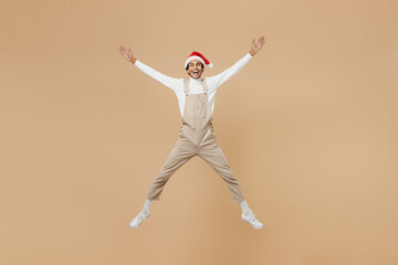 Fototapeta na wymiar Full body surprised young african man 20s wear Santa Claus red Christmas hat jump high with outstretched hands isolated on plain pastel beige background studio Happy New Year 2022 celebration concept.