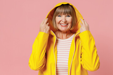 Excited happy mature elderly woman 55 years old wears yellow waterproof raincoat hold the hood...