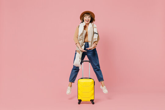 Full Size Body Length Traveler Tourist Mature Elderly Senior Lady Woman 55 Years Old Wear Casual Clothes Hat Scarf Hold Suitcase Bag Jump Isolated Plain Pastel Light Pink Background Studio Portrait