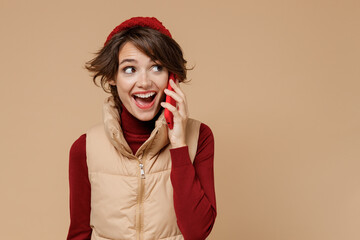 Young woman 20s wears red turtleneck vest beret talk speak on mobile cell phone conducting pleasant...