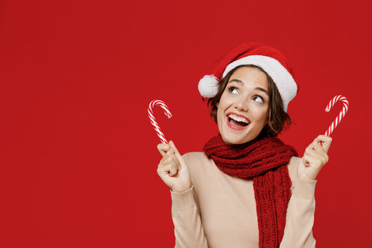 Young smiling fun happy woman 20s in Santa Claus Christmas red hat hold candy cane stick lollipop look aside isolated on plain red background studio portrait. Happy New Year 2022 celebration concept - Powered by Adobe