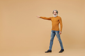 Full body elderly gray-haired mustache bearded man 50s in mustard yellow turtleneck shirt point index finger aside on workspace area mock up isolated on plain pastel beige background studio portrait