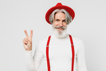 Fototapeta na wymiar Elderly smiling happy gray-haired mustache bearded man 50s in turtleneck red hat suspenders look camera show victory sign isolated on plain white background studio portrait. People lifestyle concept.