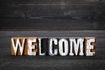 Welcome. White wooden letters on a dark wooden background