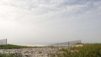 Wooden picket fence, sandy misty beach, Encinitas California USA. Pacific ocean coast, dense fog on empty sea shore. Coastline near Los Angeles, boards in milky smog haze. Gloomy weather on shoreline.