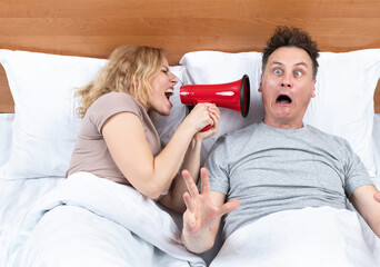 Couple in bed, a woman shouts into a red megaphone at a man who wakes up with fright in his eyes....