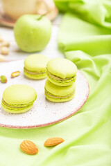 Green macarons or macaroons cakes with cup of coffee on a white wooden background. Side view, selective focus.