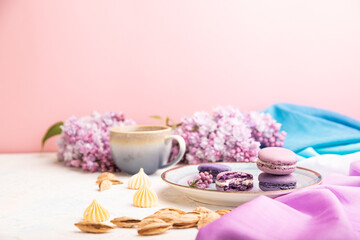 Fototapeta na wymiar Purple macarons or macaroons cakes with cup of coffee on a white and pink background. Side view, selective focus, copy space.