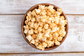Popcorn with caramel in wooden bowl on a white wooden background. Top view.