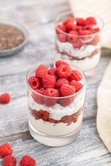 Yogurt with raspberry, goji berries and chia seeds in glass on gray wooden background. Side view, selective focus.