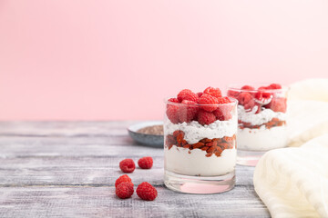 Yogurt with raspberry, goji berries and chia seeds in glass on gray and pink background. Side view, copy space.