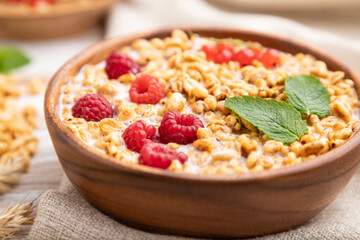 Wheat flakes porridge with milk, raspberry and currant in wooden bowl on white wooden background. Side view, selective focus.