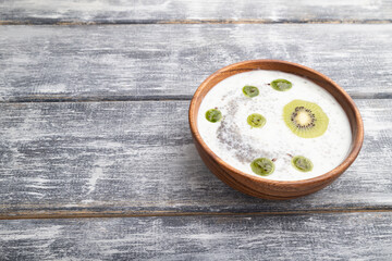 Yogurt with kiwi, gooseberry, chia and almonds in wooden bowl on gray wooden background. side view, copy space.