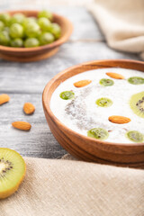 Yogurt with kiwi, gooseberry, chia and almonds in wooden bowl on gray wooden background. Side view, close up, selective focus.