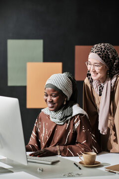 Two muslim businesswomen working together at the table at office they looking at computer monitor and laughing