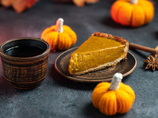 A piece of homemade pumpkin pie for Thanksgiving, a cup of coffee and knitted orange pumpkins
