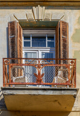 Window with open shutters in front of a small balcony with metal grille	