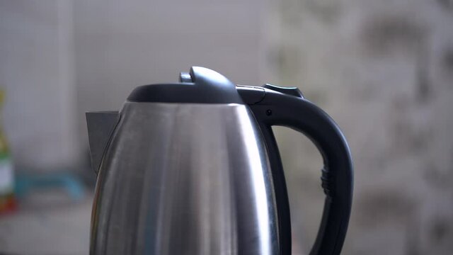 Button for turning on the electric kettle for boiling water. An electric kettle boils water. Person turns on the electric kettle.