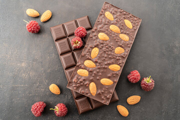 assortment chocolate bars with almonds, raspberries, handmade sweets. Composition of bars milk and dark almond chocolate, raspberries on a black background, top view. Pastry craft on the table