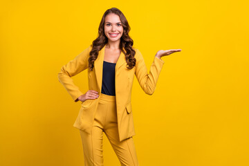 Portrait of attractive cheerful wavy-haired woman agent broker holding on palm copy space isolated over vivid yellow color background