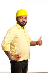 Young Indian engineer wearing yellow color hard hat and showing thumps up on white background.