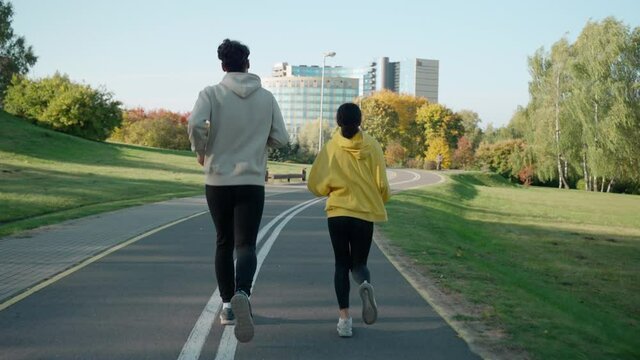 Man and woman start running on a track at the park in autumn, talking and smiling. Couple of young people starting a morning run. Running with a partner talking. High quality 4k footage