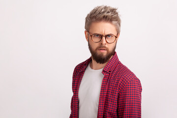 Portrait of puzzled blond bearded man wearing eyeglasses frowning and seriously looking at camera. Indoor studio shot isolated on gray background
