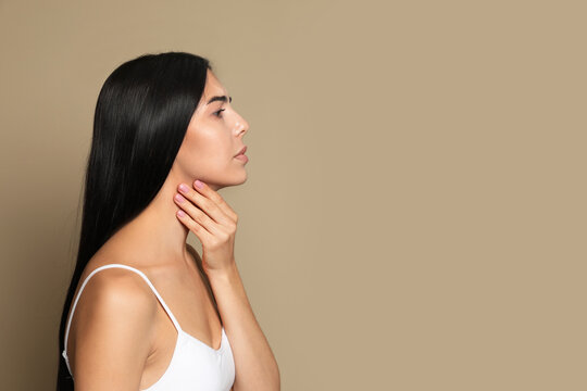 Young woman doing thyroid self examination on beige background. Space for text