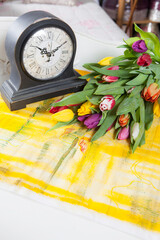 A bouquet of multicolored tulips lies on the table next to the old table clock