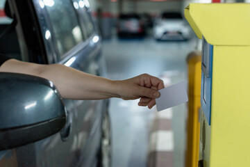 Caucasian woman driving her car approaches her hand with white security card to access the parking lot to the control machine and open the barriers.