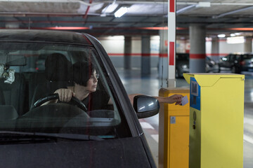 Adult Caucasian woman driving her car opens the barrier of a subway indoor parking garage with the...