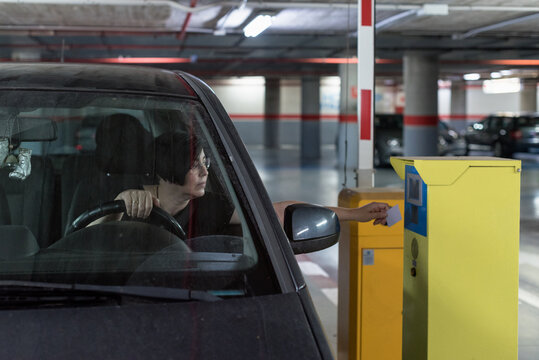 Adult Caucasian woman driving her car opens the barrier of a subway indoor parking garage with the security card.