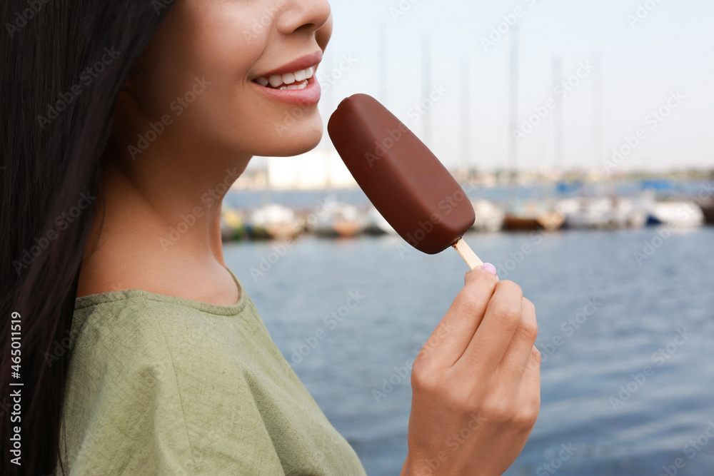 Wall mural young woman eating ice cream glazed in chocolate near river, closeup