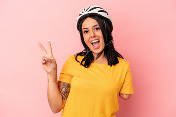 Young caucasian woman with one arm wearing a bike helmet isolated on pink background joyful and carefree showing a peace symbol with fingers.