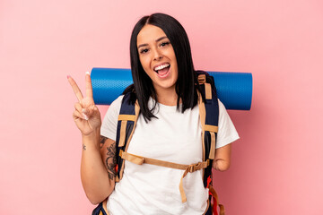 Young caucasian hiker woman with one arm isolated on pink background joyful and carefree showing a peace symbol with fingers.