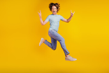 Fototapeta na wymiar Full-body photo of young cheerful man show fingers horns rock sign jump rude isolated on shine yellow background