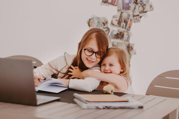 Fototapeta na wymiar Smart little girl wearing eyeglasses, sitting at table, using notebook, studying at home.
