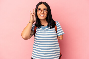 Young caucasian student woman with one arm isolated on pink background trying to listening a gossip.