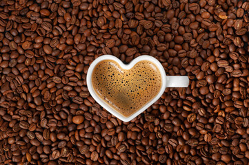 Coffee with a beautiful froth in a mug in the shape of a heart on a background of coffee beans. copy space