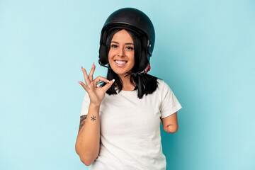Young caucasian woman with one arm wearing a motorcycle helmet isolated o blue background cheerful and confident showing ok gesture.