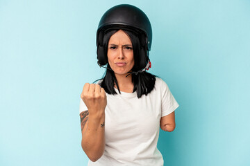 Young caucasian woman with one arm wearing a motorcycle helmet isolated o blue background showing fist to camera, aggressive facial expression.
