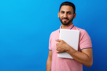 Portrait of positive man standing and holding laptop against blue background