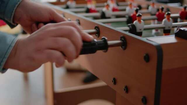 Close up of man playing soccer game at foosball table after work. Businessman enjoying football game at office after hours, celebrating party with colleagues, having fun with friends