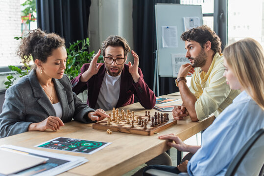 Shocked businessman sitting near multiethnic colleagues playing chess in office