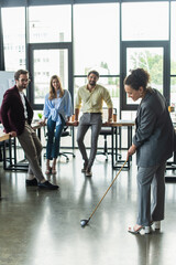 Fototapeta na wymiar African american businesswoman playing golf near colleagues in office