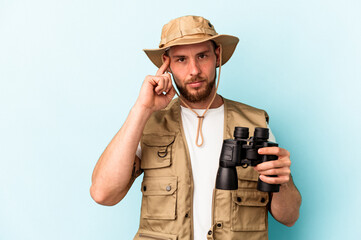 Young caucasian man looking at animals through binoculars isolated on blue background pointing temple with finger, thinking, focused on a task.