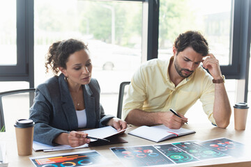 Interracial business people working with charts on papers near coffee to go in office