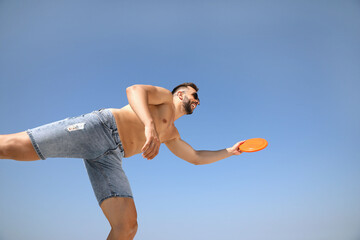 Happy man catching flying disk against blue sky on sunny day, low angle view