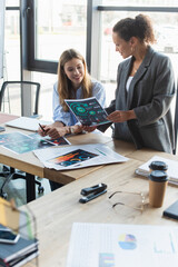 Smiling african american businesswoman holding paper near cheerful colleague near coffee to go and documents in office
