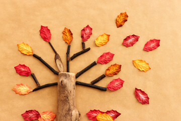 Concept image of handmade wooden tree and autumn leaves on brown recycled paper background